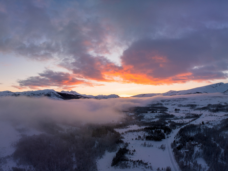 Aerial view of the snowy winter landscape on Kvaloya island featuring rolling hills covered in snow low hanging clouds and a vibrant sunset sky in Troms Norway.