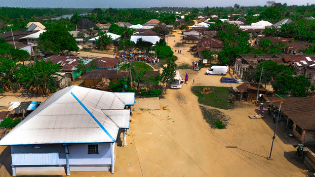 Aerial view of the village with dirt roads metal roofed houses lush vegetation and a white van parked near a gathering of people in Abua Rivers Nigeria. Aerial view of the village with dirt roads metal roofed houses lush vegetation and a white van parked near a gathering of people in Abua Rivers Nigeria.