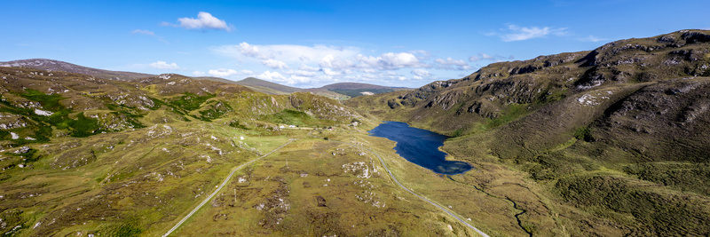 Aerial view of the rugged landscape of An Port featuring a deep blue lake surrounded by rolling green hills and winding roads in Ardara County Donegal Ireland.