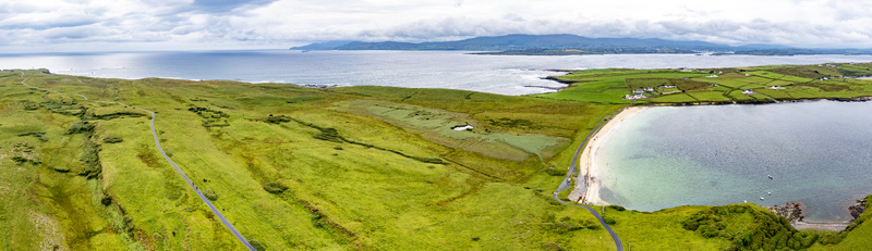 Aerial view of St John s Point Beach featuring lush green coastal fields a winding road and the Atlantic Ocean under a cloudy sky in Dunkineely County Donegal Ireland.