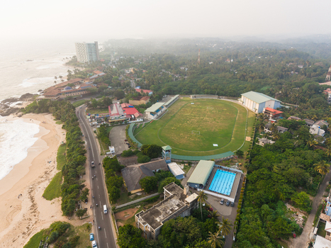 Aerial view of a sports complex featuring a football field and swimming pool along the coastal road and sandy beach in Galle Southern Province Sri Lanka.