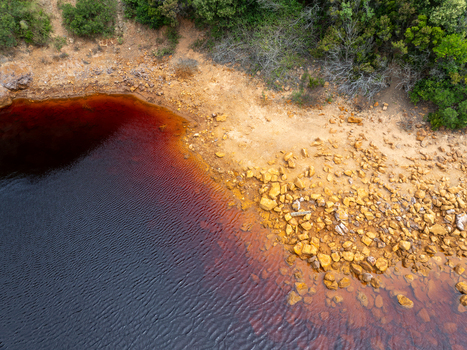 Aerial view of the unique red waters of Laghetto delle conche also known as Lago di sangue surrounded by rocky terrain and Mediterranean vegetation in Rio Marina Toscana Italy.