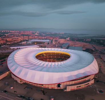 Aerial view of Riyadh Air Metropolitano Stadium with its distinctive white roof and illuminated bowl set against the urban landscape of Madrid Comunidad de Madrid Spain.