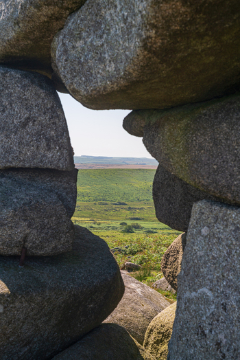 View of the Cheesewring granite rock formation framing the rolling green hills and moorland landscape of Minions Cornwall United Kingdom. View of the Cheesewring granite rock formation framing the rolling green hills and moorland landscape of Minions Cornwall United Kingdom.