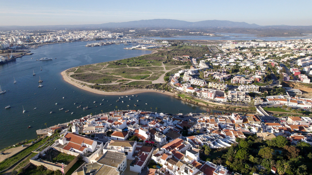 Aerial view of the coastal town of Ferragudo featuring traditional white washed houses a scenic river estuary small fishing boats and the surrounding landscape in Ferragudo Faro District Portugal.
