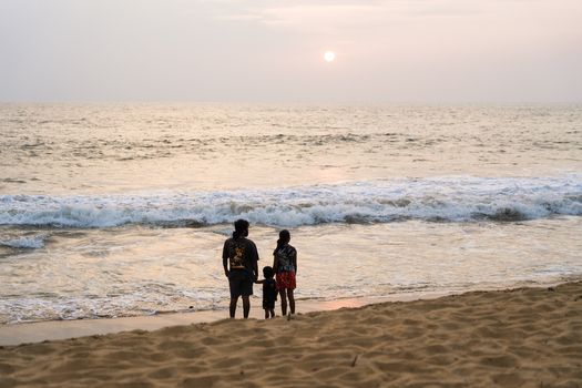 Sri Lanka 16 January 2026 View of a family standing on a sandy beach watching the sunset over the crashing waves of the Indian Ocean.