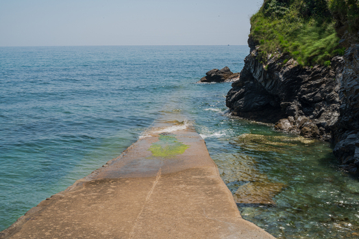 View of a concrete slipway extending into the calm sea beside rugged cliffs in Charlestown Cornwall United Kingdom. View of a concrete slipway extending into the calm sea beside rugged cliffs in Charlestown Cornwall United Kingdom.
