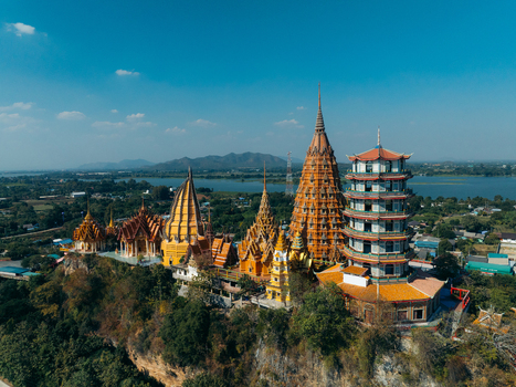 Aerial view of Wat Tham Suea temple complex with its golden pagodas and ornate architecture on a hilltop overlooking the river and mountains in Muang Chum Kanchanaburi Thailand. Aerial view of Wat Tham Suea temple complex with its golden pagodas and ornate architecture on a hilltop overlooking the river and mountains in Muang Chum Kanchanaburi Thailand.