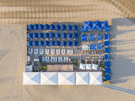 Aerial view of a beach club with rows of blue umbrellas and white sun loungers arranged on the sand in La Grande Motte Occitanie France.