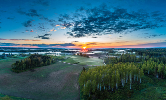 Aerial view of a rural landscape with lush forests agricultural fields and morning mist under a vibrant sunrise sky in Latvia. Aerial view of a rural landscape with lush forests agricultural fields and morning mist under a vibrant sunrise sky in Latvia.