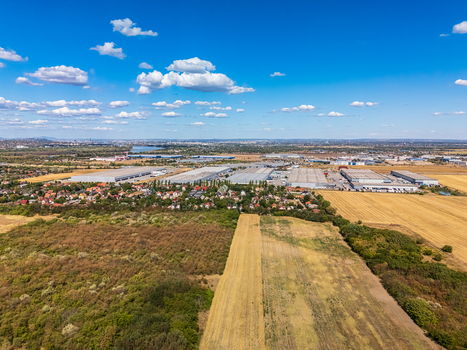 Aerial view of a large logistics park with industrial warehouses situated near residential areas and agricultural fields under a bright blue sky in Szigetszentmiklos Pest County Hungary. Aerial view of a large logistics park with industrial warehouses situated near residential areas and agricultural fields under a bright blue sky in Szigetszentmiklos Pest County Hungary.
