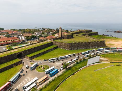Aerial view of Galle Fort featuring the historic clock tower and massive stone ramparts with buses lined up on the road below in Galle Southern Province Sri Lanka. Aerial view of Galle Fort featuring the historic clock tower and massive stone ramparts with buses lined up on the road below in Galle Southern Province Sri Lanka.