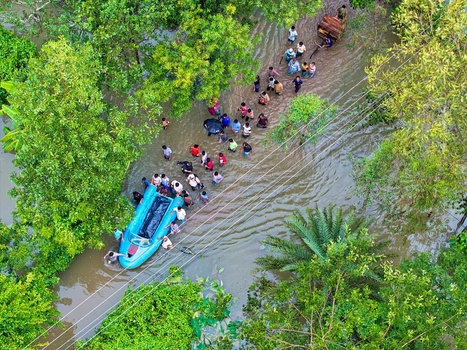 Banshkhali Upazila Bangladesh 10 July 2026 Aerial view of people wading through floodwaters alongside a small boat in a submerged rural area surrounded by lush trees. Banshkhali Upazila Bangladesh 10 July 2026 Aerial view of people wading through floodwaters alongside a small boat in a submerged rural area surrounded by lush trees.