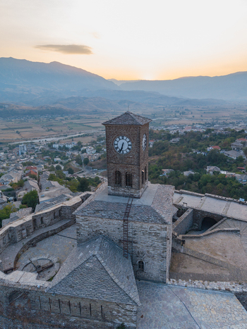 Aerial view of the historic Gjirokaster Fortress clock tower with its stone masonry and surrounding mountain landscape at sunset in Gjirokaster Gjirokaster County Albania. Aerial view of the historic Gjirokaster Fortress clock tower with its stone masonry and surrounding mountain landscape at sunset in Gjirokaster Gjirokaster County Albania.