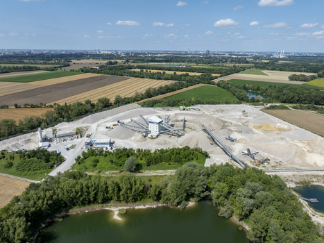 Aerial view of a gravel plant with conveyor belts and piles of processed stone situated near a pond and agricultural fields in Aschheim Bavaria Germany.