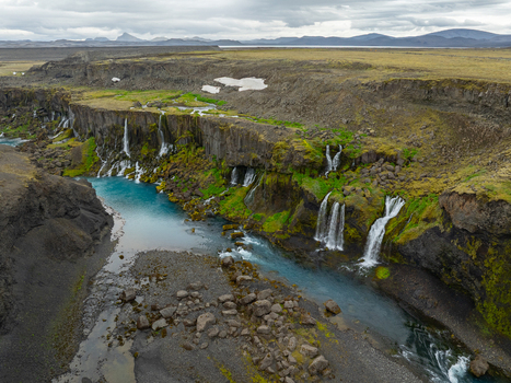 Aerial view of Sigoldugljufur canyon featuring multiple waterfalls cascading into a turquoise river surrounded by mossy cliffs and rocky terrain in Rangarthing ytra Iceland. Aerial view of Sigoldugljufur canyon featuring multiple waterfalls cascading into a turquoise river surrounded by mossy cliffs and rocky terrain in Rangarthing ytra Iceland.