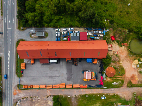 Aerial view of a large industrial warehouse with a red roof surrounded by a parking lot with vehicles construction materials and trees in Zebrak Central Bohemian Region Czechia. Aerial view of a large industrial warehouse with a red roof surrounded by a parking lot with vehicles construction materials and trees in Zebrak Central Bohemian Region Czechia.