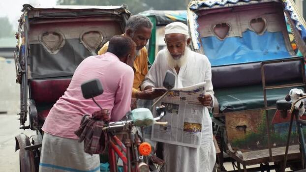 View of men reading a newspaper between rickshaws Bangladesh.