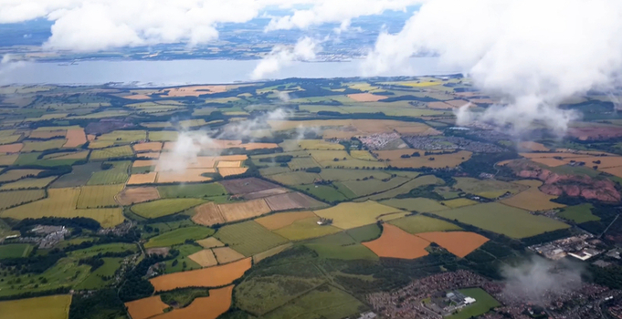 Aerial view of agricultural fields with patches of green and brown crops scattered clouds and a distant coastline in Kings County New York United States. Aerial view of agricultural fields with patches of green and brown crops scattered clouds and a distant coastline in Kings County New York United States.