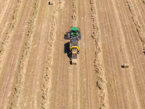 Aerial view of a green tractor pulling a baler through a harvested field with rows of hay and scattered hay bales in Philadelphia Western Cape South Africa. Aerial view of a green tractor pulling a baler through a harvested field with rows of hay and scattered hay bales in Philadelphia Western Cape South Africa.