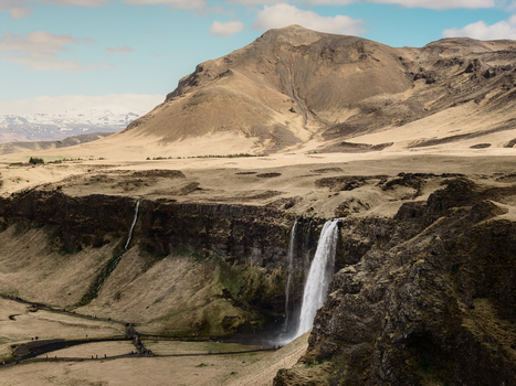 Aerial view of Seljalandsfoss waterfall cascading over rocky cliffs into a lush green valley surrounded by vast volcanic plains and distant mountains in Rangarthing eystra Iceland. Aerial view of Seljalandsfoss waterfall cascading over rocky cliffs into a lush green valley surrounded by vast volcanic plains and distant mountains in Rangarthing eystra Iceland.