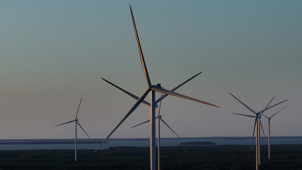 Aerial view of Metsalamminkangas Tuulipuisto wind farm with large turbines above the forest and distant water under golden hour light in Siikalatva Pohjois Pohjanmaa Finland. Aerial view of Metsalamminkangas Tuulipuisto wind farm with large turbines above the forest and distant water under golden hour light in Siikalatva Pohjois Pohjanmaa Finland.