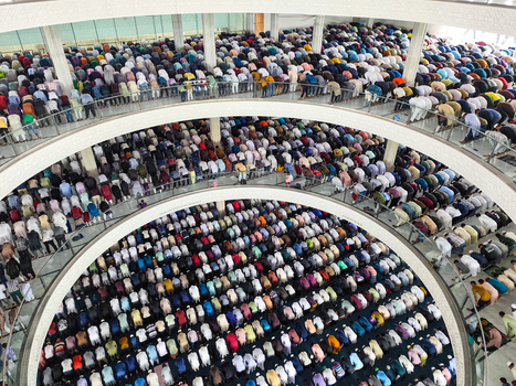 Dhaka Bangladesh 19 June 2026 Aerial view of a large crowd of men praying in rows inside a multi level mosque with architectural balconies and bright interior lighting.