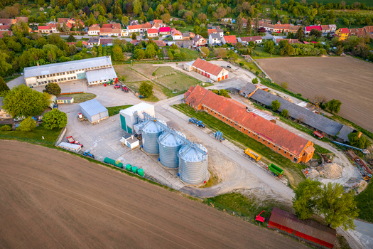 Aerial view of an agricultural farm with grain silos long red roofed barns and tractors surrounded by green fields in Chvalkovice Hradec Kralove Region Czechia.