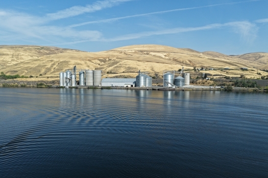 Aerial view of a grain elevator facility with large metal silos situated along the riverbank surrounded by rolling golden hills in Whitman County Washington United States. Aerial view of a grain elevator facility with large metal silos situated along the riverbank surrounded by rolling golden hills in Whitman County Washington United States.