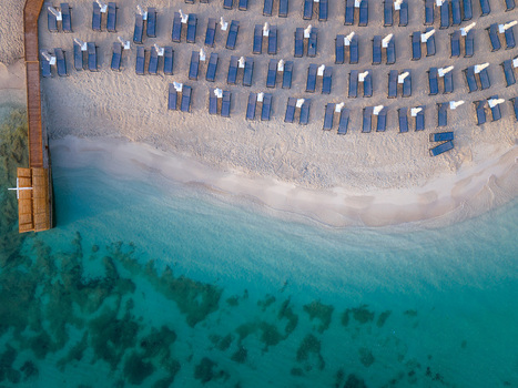 Aerial view of rows of blue sunbeds and white umbrellas on a sandy beach by turquoise water in Ksamil Vlore County Albania. Aerial view of rows of blue sunbeds and white umbrellas on a sandy beach by turquoise water in Ksamil Vlore County Albania.