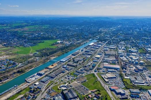 Aerial view of the shimmering Canal du Rh&ocirc;ne au Rhin cuts a tranquil path through the urban and industrial sprawl contrasting with the lush green fields beyond Sausheim Grand Est France.