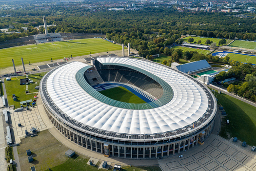 Berlin Germany 26 September 2026 Aerial view of the Olympiastadion Berlin featuring its iconic oval roof blue running track and surrounding green parkland on a clear day.