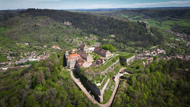 Aerial view of Fort Saint Andre featuring its historic stone walls and buildings surrounded by lush green hills and forests in Salins les Bains Bourgogne Franche Comte France. Aerial view of Fort Saint Andre featuring its historic stone walls and buildings surrounded by lush green hills and forests in Salins les Bains Bourgogne Franche Comte France.