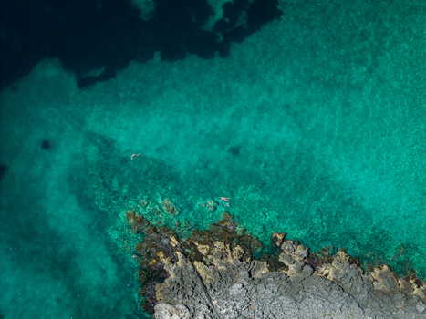 Aerial view of Aquarium Beach with swimmers in crystal clear turquoise water along the rugged rocky coastline in Jala Vlore County Albania. Aerial view of Aquarium Beach with swimmers in crystal clear turquoise water along the rugged rocky coastline in Jala Vlore County Albania.