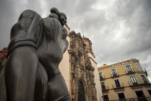 View of a bronze statue in the foreground with the ornate colonial facade of a historic church and surrounding buildings under a cloudy sky in Guanajuato Guanajuato Mexico. View of a bronze statue in the foreground with the ornate colonial facade of a historic church and surrounding buildings under a cloudy sky in Guanajuato Guanajuato Mexico.