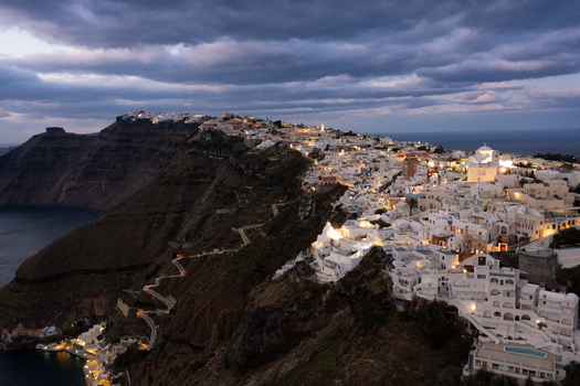 Aerial view of the white buildings cascade down the cliffside towards the sea a stark contrast against the dark volcanic rock Fira Thira Greece. Aerial view of the white buildings cascade down the cliffside towards the sea a stark contrast against the dark volcanic rock Fira Thira Greece.
