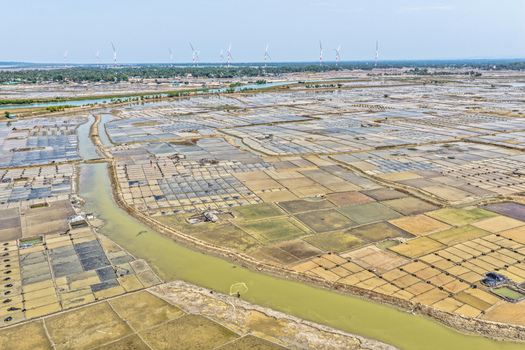 Aerial view of geometric salt farms shimmering under the sun s glare contrasted by the serene river and distant wind turbines Cox s Bazar Chittagong Division Bangladesh. Aerial view of geometric salt farms shimmering under the sun s glare contrasted by the serene river and distant wind turbines Cox s Bazar Chittagong Division Bangladesh.