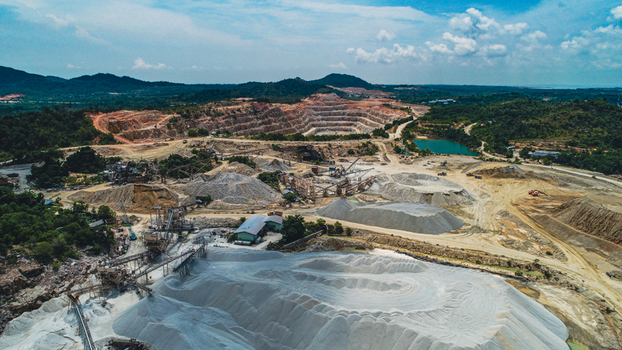 Aerial view of a sand mining quarry with heavy machinery piles of extracted sand and industrial equipment near lush hills in Karimun Kepulauan Riau Indonesia. Aerial view of a sand mining quarry with heavy machinery piles of extracted sand and industrial equipment near lush hills in Karimun Kepulauan Riau Indonesia.