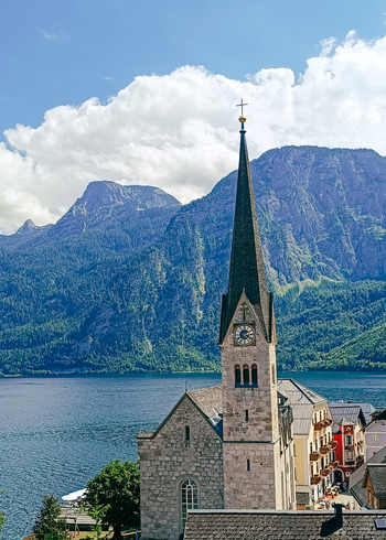 View of the Evangelical Church of Hallstatt with its stone tower and clock face overlooking Hallstatt Lake against a backdrop of mountains in Hallstatt Upper Austria Austria. View of the Evangelical Church of Hallstatt with its stone tower and clock face overlooking Hallstatt Lake against a backdrop of mountains in Hallstatt Upper Austria Austria.