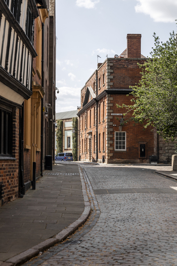 View of a historic cobblestone street lined with traditional red brick buildings and timber framed architecture under a clear blue sky in Coventry England United Kingdom.