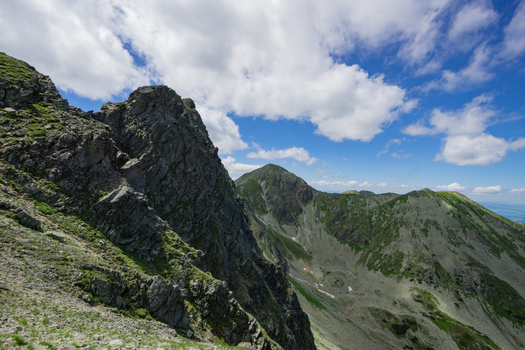 View of Tri kopy peaks in the Western Tatras featuring jagged rocky ridges and steep green slopes under a blue sky with white clouds in Ziar Zilina Region Slovakia. View of Tri kopy peaks in the Western Tatras featuring jagged rocky ridges and steep green slopes under a blue sky with white clouds in Ziar Zilina Region Slovakia.