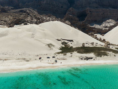 Aerial view of pristine white sand dunes meet the turquoise waters near the rugged mountains creating a striking contrast of textures and tones Erissel Socotra Yemen.