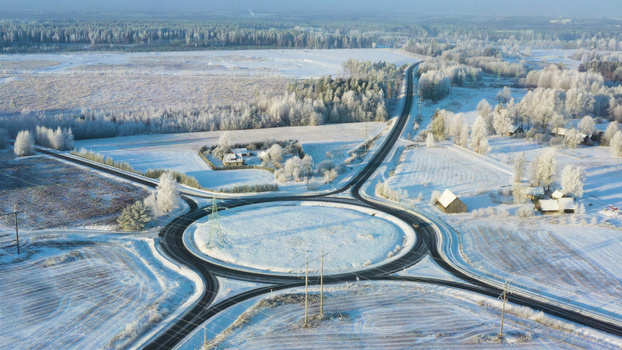 Aerial view of a roundabout surrounded by snow covered fields and frost covered trees in the rural landscape of Latvia. Aerial view of a roundabout surrounded by snow covered fields and frost covered trees in the rural landscape of Latvia.