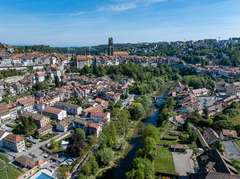 Aerial view of St Nicolas Cathedral and the historic old town with the Sarine river flowing through lush greenery and traditional red roofed buildings in Fribourg Fribourg Switzerland. Aerial view of St Nicolas Cathedral and the historic old town with the Sarine river flowing through lush greenery and traditional red roofed buildings in Fribourg Fribourg Switzerland.