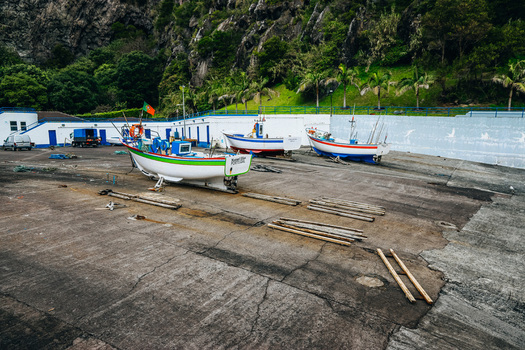 View of fishing boats resting on a sun drenched concrete pier showcasing vibrant colors against the backdrop of lush green cliffs Caloura A&ccedil;ores Portugal.