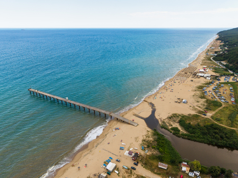 Aerial view of the wooden pier extending into the Black Sea at the sandy beach with beach umbrellas and a river mouth in Shkorpilovtsi Varna Bulgaria. Aerial view of the wooden pier extending into the Black Sea at the sandy beach with beach umbrellas and a river mouth in Shkorpilovtsi Varna Bulgaria.