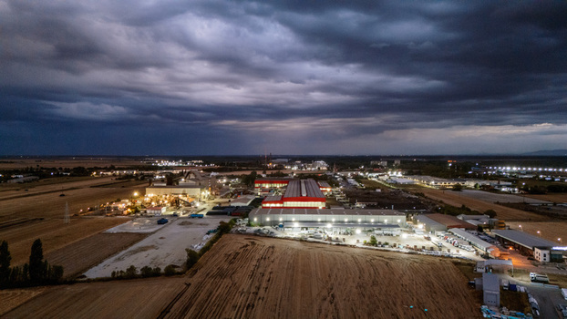 Aerial view of an illuminated industrial facility with large warehouses and surrounding agricultural fields under a dramatic dark storm sky in Sremska Mitrovica Vojvodina Serbia. Aerial view of an illuminated industrial facility with large warehouses and surrounding agricultural fields under a dramatic dark storm sky in Sremska Mitrovica Vojvodina Serbia.