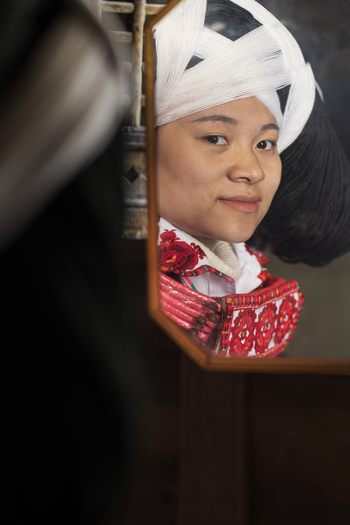 Gaoxing China 30 April 2026 View of a Long Horn Miao woman in traditional embroidered dress and large yarn headpiece looking at her reflection in a mirror. Gaoxing China 30 April 2026 View of a Long Horn Miao woman in traditional embroidered dress and large yarn headpiece looking at her reflection in a mirror.