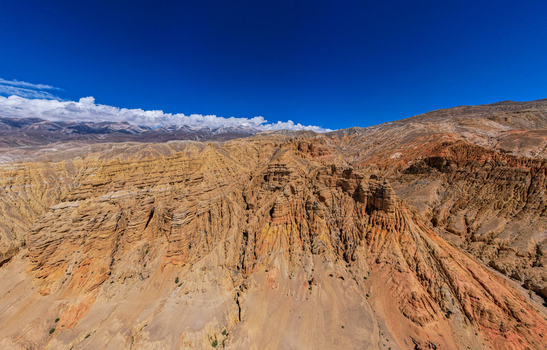 Aerial view of the arid rugged and layered rock formations of the Mustang region with deep canyons under a clear blue sky in Nepal.