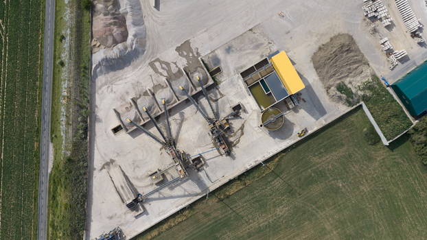 Aerial view of an industrial aggregate processing plant with conveyor belts gravel piles and settling tanks situated in a rural landscape in La Longueville Hauts de France France.